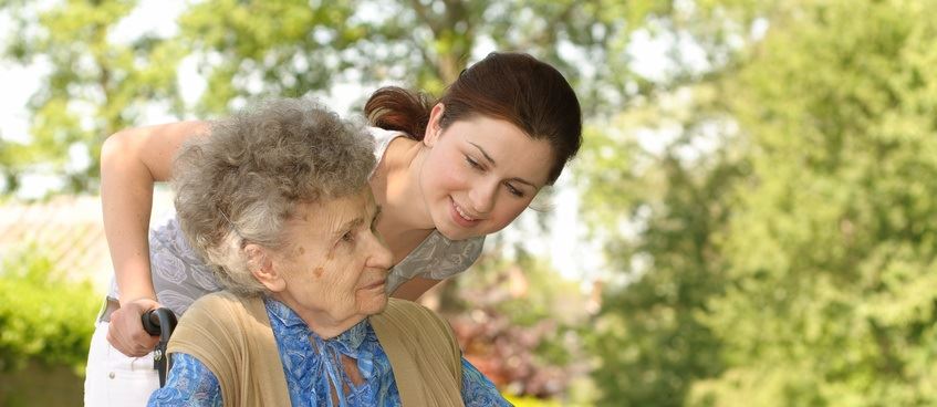 Pflegekraft unterstützt eine ältere Dame im Garten